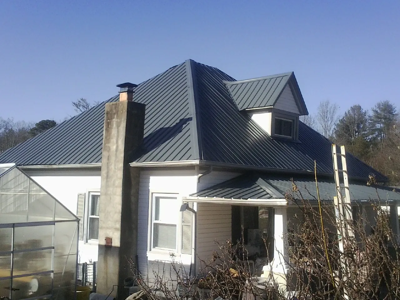 Dark blue standing seam metal roof on a white farmhouse with dormer — Slate & Tile Roof Repair by Roofing Brothers in Long Branch