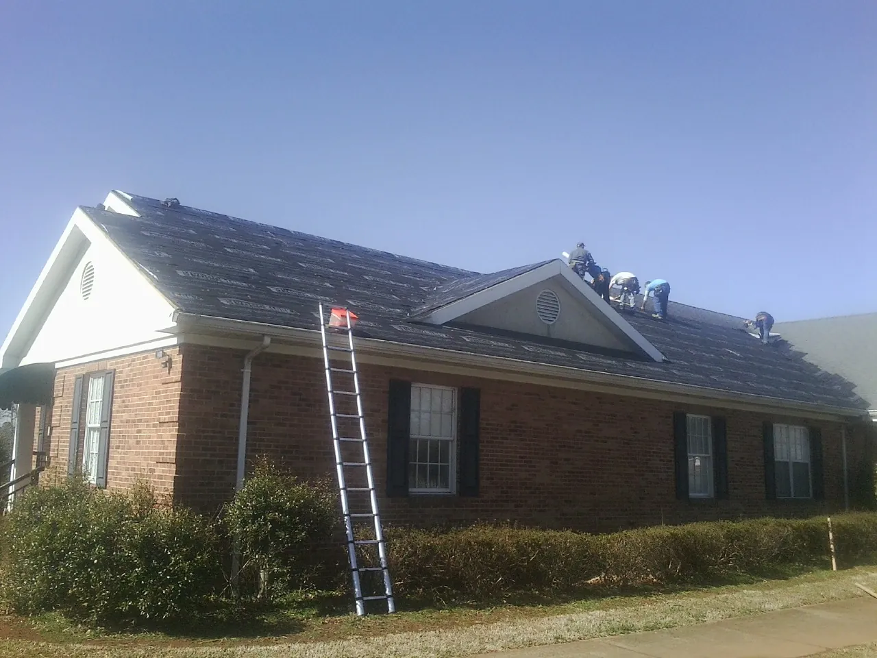 Crew tearing shingles off a brick ranch roof with a ladder set — Metal Roof Repair work by our crew in Long Branch