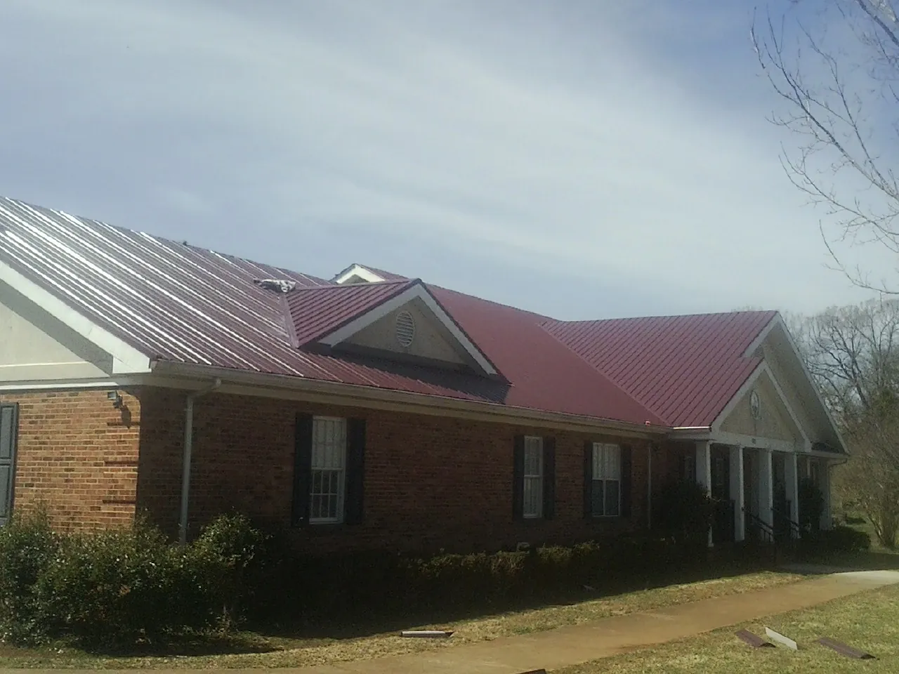 Red metal roof with gabled entries on a long brick building, from a Hail Damage Roof Repair job in Long Branch
