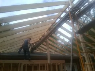 Rafters going up over a new addition with a worker on the wall in Long Branch