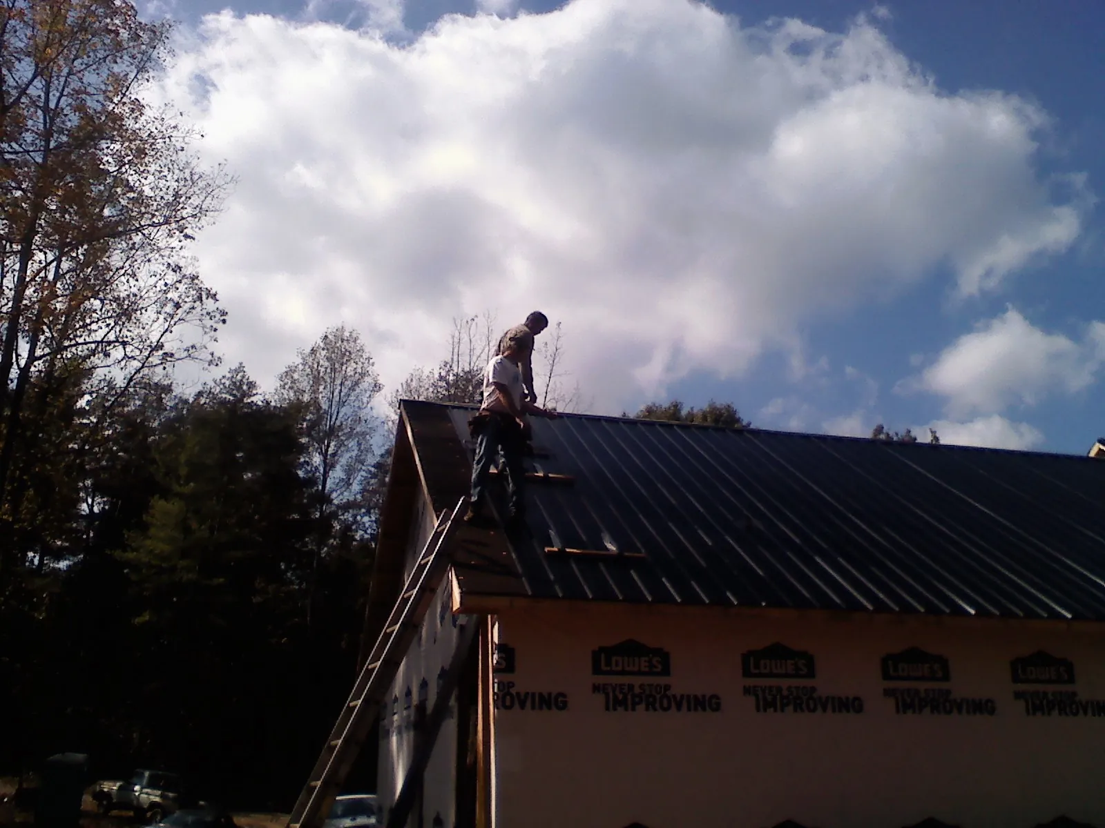 Roofer fastening dark metal panels high against a cloudy sky, from a Roof Inspection job in Long Branch