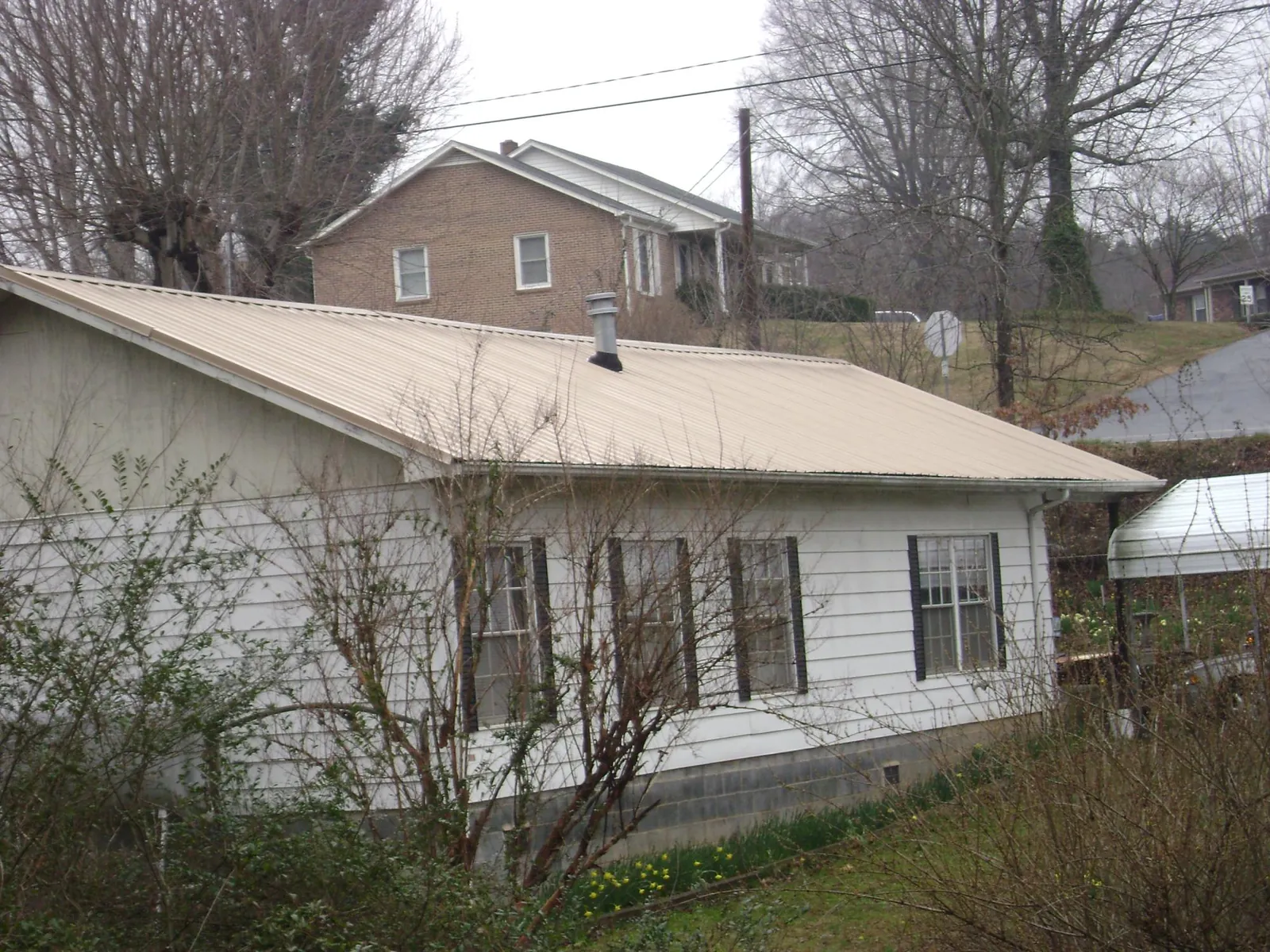 Tan metal roof on a white sided house set into a hillside — Commercial Roofing by Roofing Brothers in Long Branch